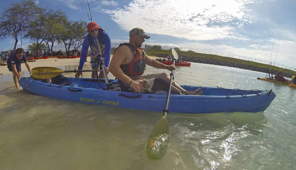 Men entering tandem fishing kayak on the shore