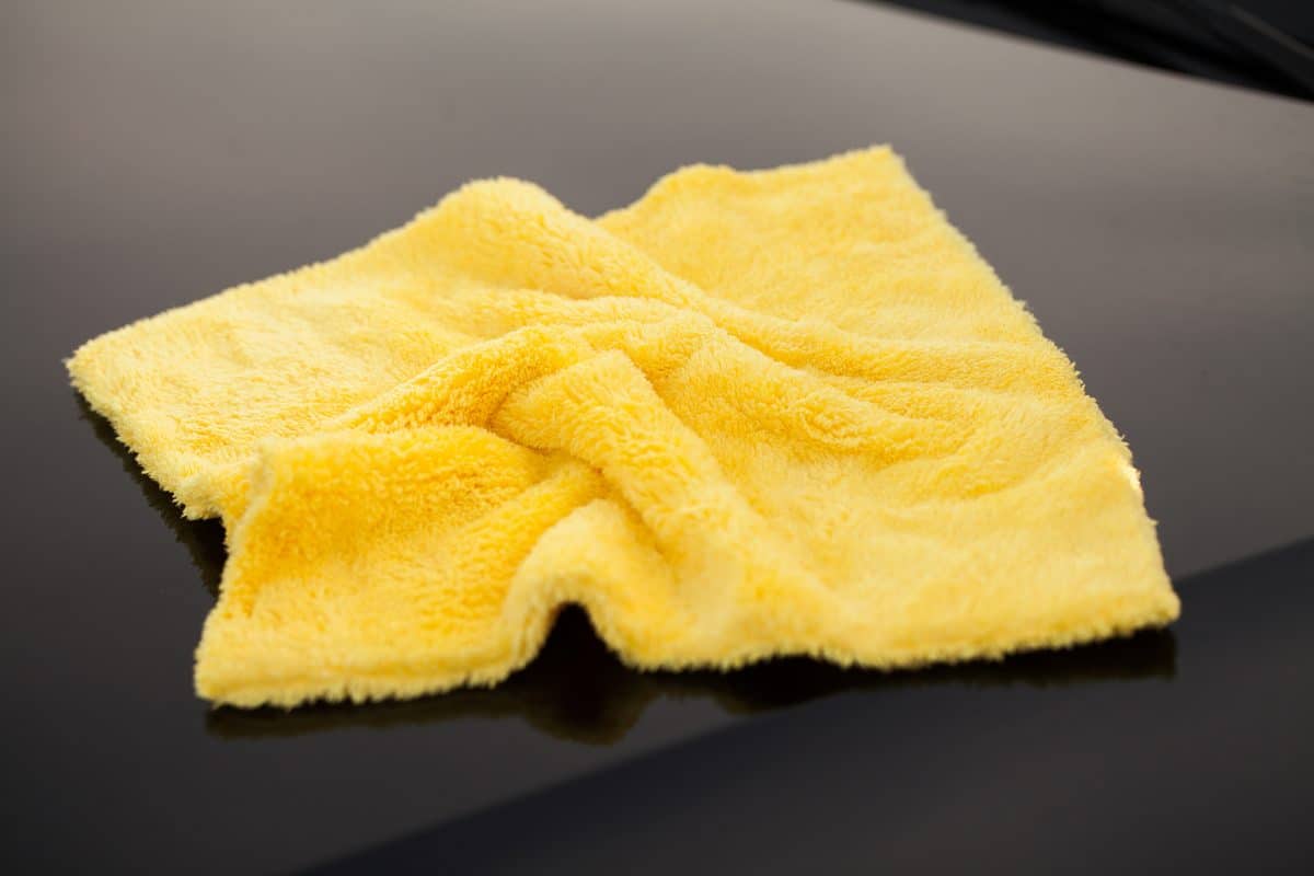 Man holds the microfiber in hand and polishes the wax off a kayak.