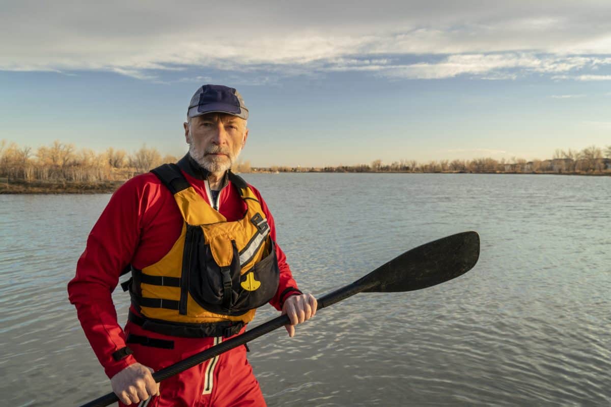 Man in red drysuit and yellow pfd holding kayak paddle