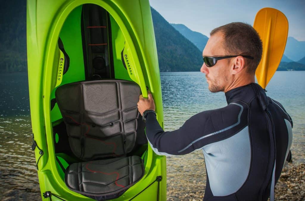 Man in wetsuit holding green kayak - Best Wetsuit For Kayaking