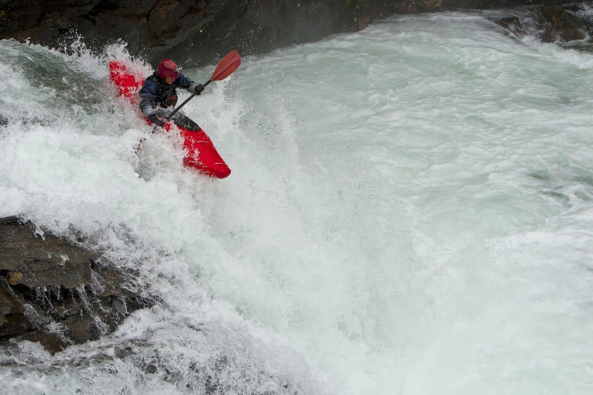 Man dropping from waterfall in red whitewater kayak