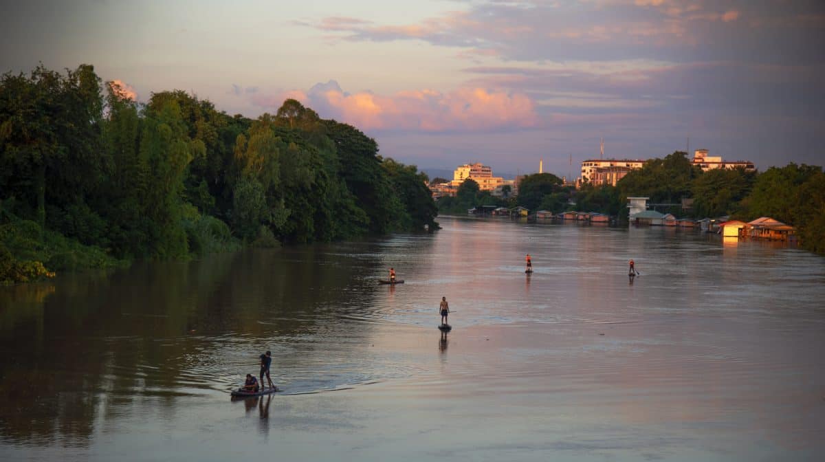 People paddle boarding on a river at sunset