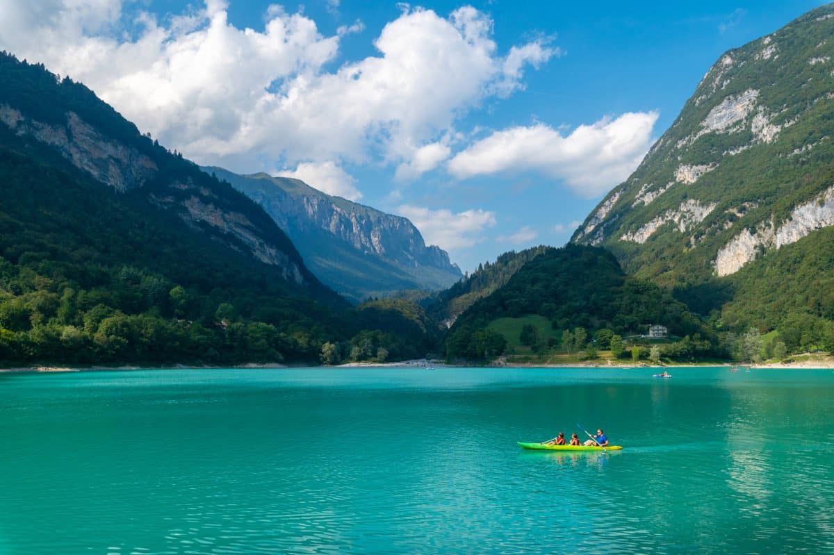 Three warm water boaters kayak in blue lake with mountain backdrop